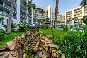 Un hotel con diversi balconi, una piscina e un giardino curato con un ruscello artificiale.