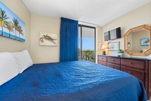 A hotel room with a large bed, a balcony with a view, a television, and a mirror.