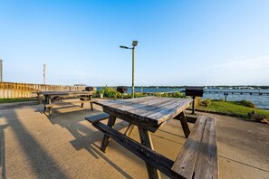 Un'area picnic all'aperto con tavoli e panchine, un lampione e vista sull'acqua.