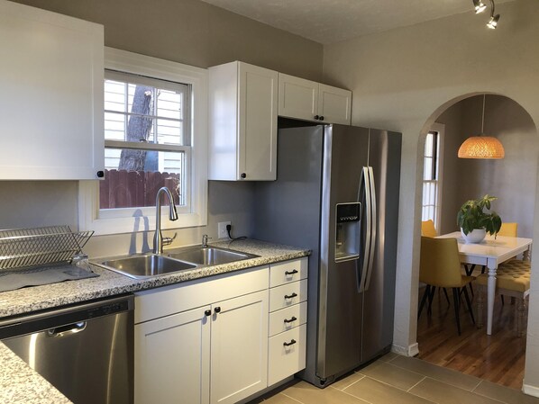 A modern kitchen with white cabinets, stainless steel appliances, a granite countertop, and a dining area with a table and chairs.
