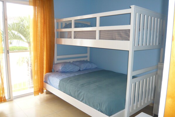 Una cama individual con cabecera azul y barandillas blancas, colcha verde y una puerta corrediza con cortinas amarillas.