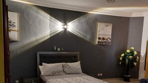 Un dormitorio con cama, mesitas de noche, lámpara de techo e imagen colgada en la pared.