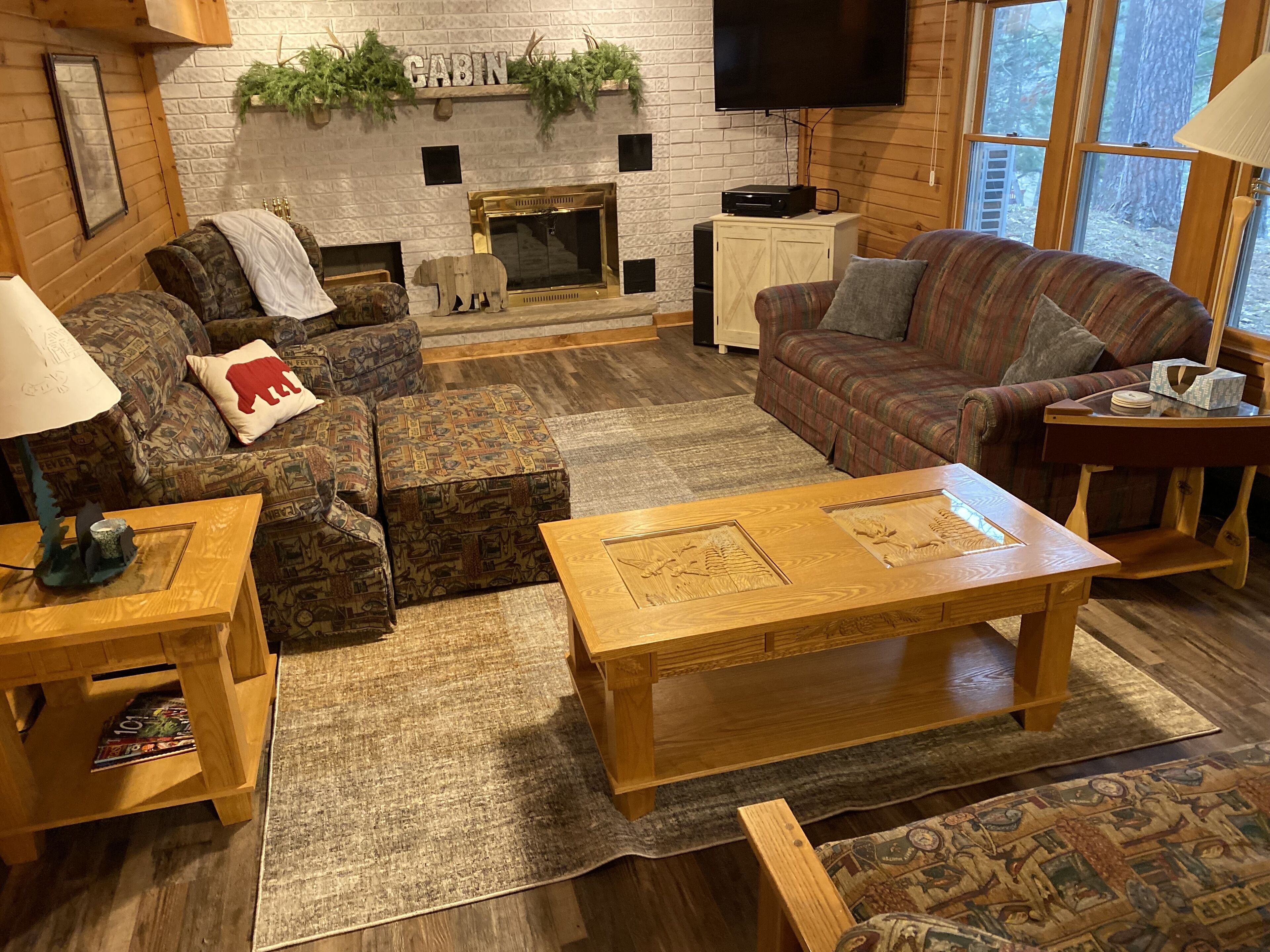 Una sala de estar acogedora de estilo cabaña con chimenea, dos sofás, una mesa de centro y una televisión.