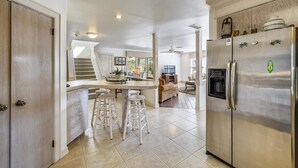 Een ruime keuken met een centraal eiland, een roestvrijstalen koelkast en een trap naar een hoger gelegen verdieping.