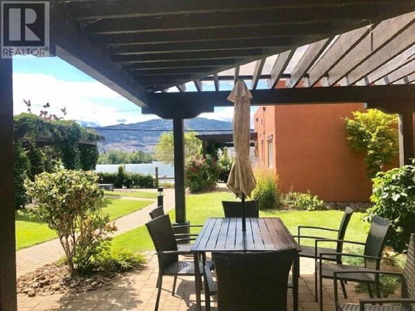 Relax in a serene outdoor space with a shaded patio, table, and chairs, surrounded by a well-manicured lawn and scenic views.