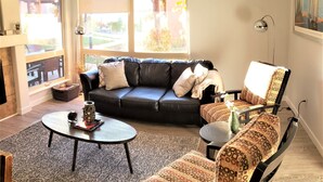 A living room with a black leather sofa, patterned armchairs, a round coffee table, and a fireplace.