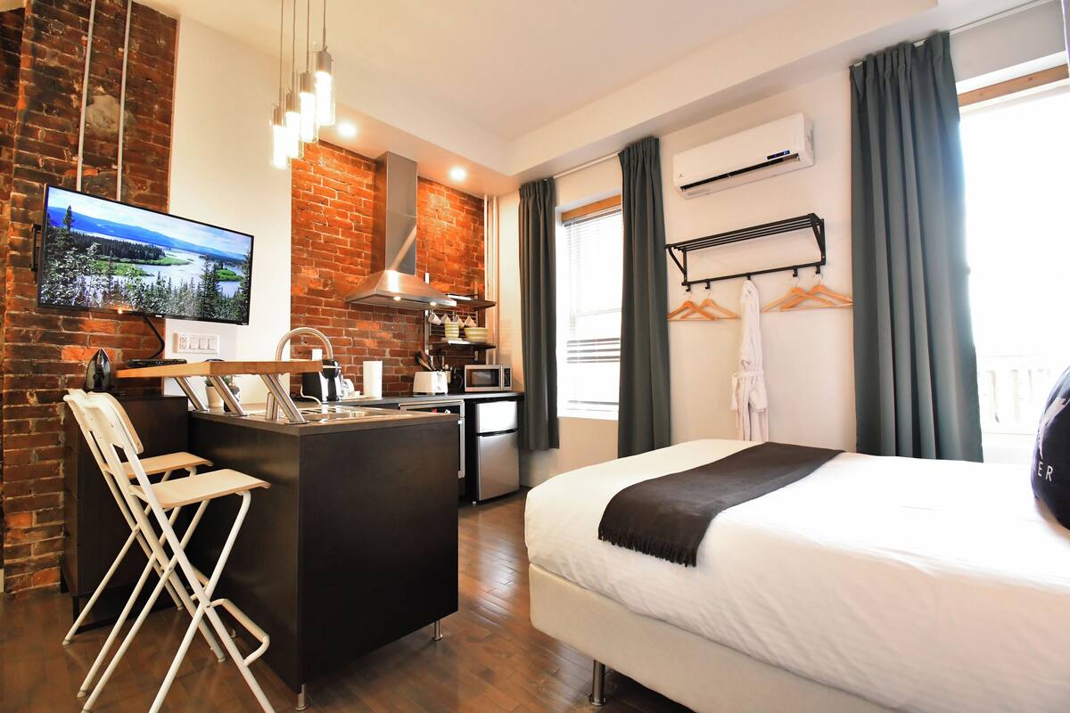Habitación de hotel moderna con cama, escritorio con televisor de pantalla plana, zona de cocina y vistas al exterior.