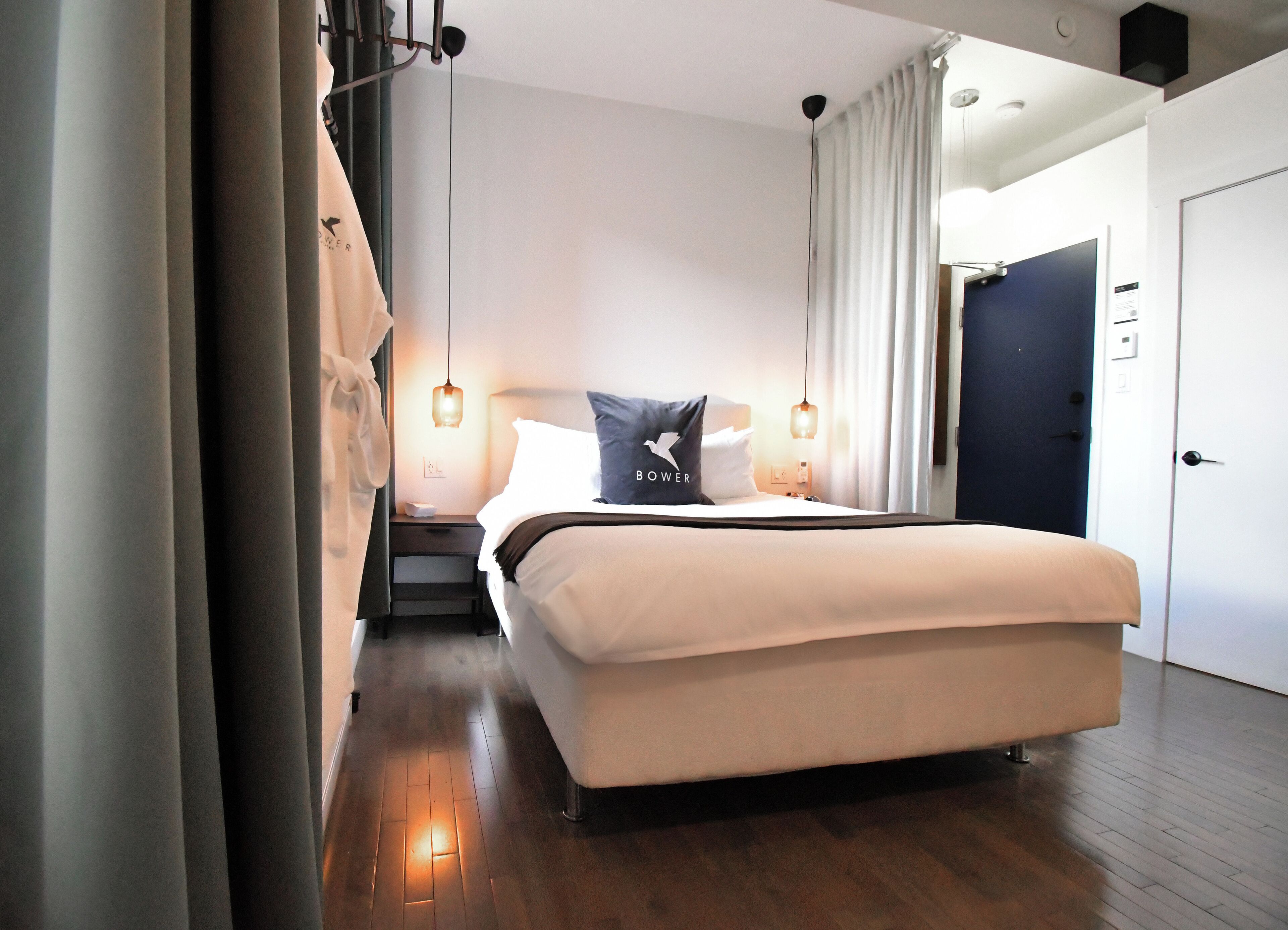 A modern hotel room with a large bed, a nightstand, a desk, and a chair. There is a door and a window in the room.