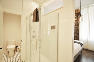 Un baño moderno con ducha de vidrio, inodoro y cama con cabecera de madera oscura.
