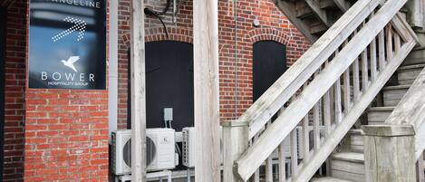 A brick building with a sign for Maison Evangeline Bower Hospitality Group, outdoor air conditioning units, and a wooden staircase.