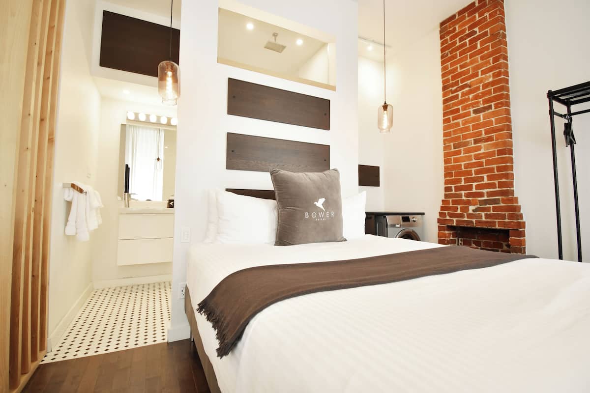 Una habitación de hotel moderna con una cama grande, una chimenea de ladrillo y un tocador con espejo e iluminación.