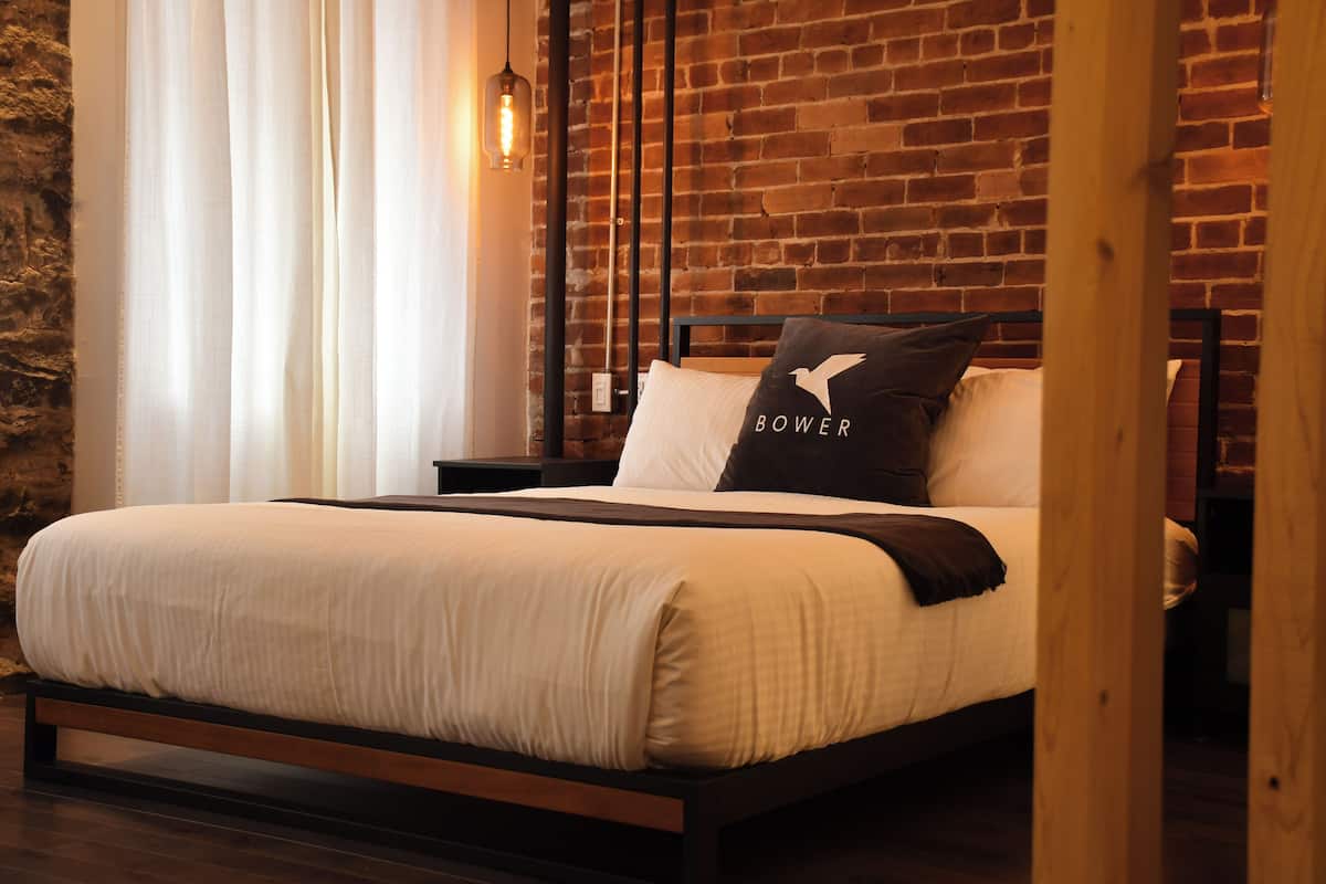 Una cama con estructura de madera, ropa de cama blanca y una almohada con la palabra "BOWER".