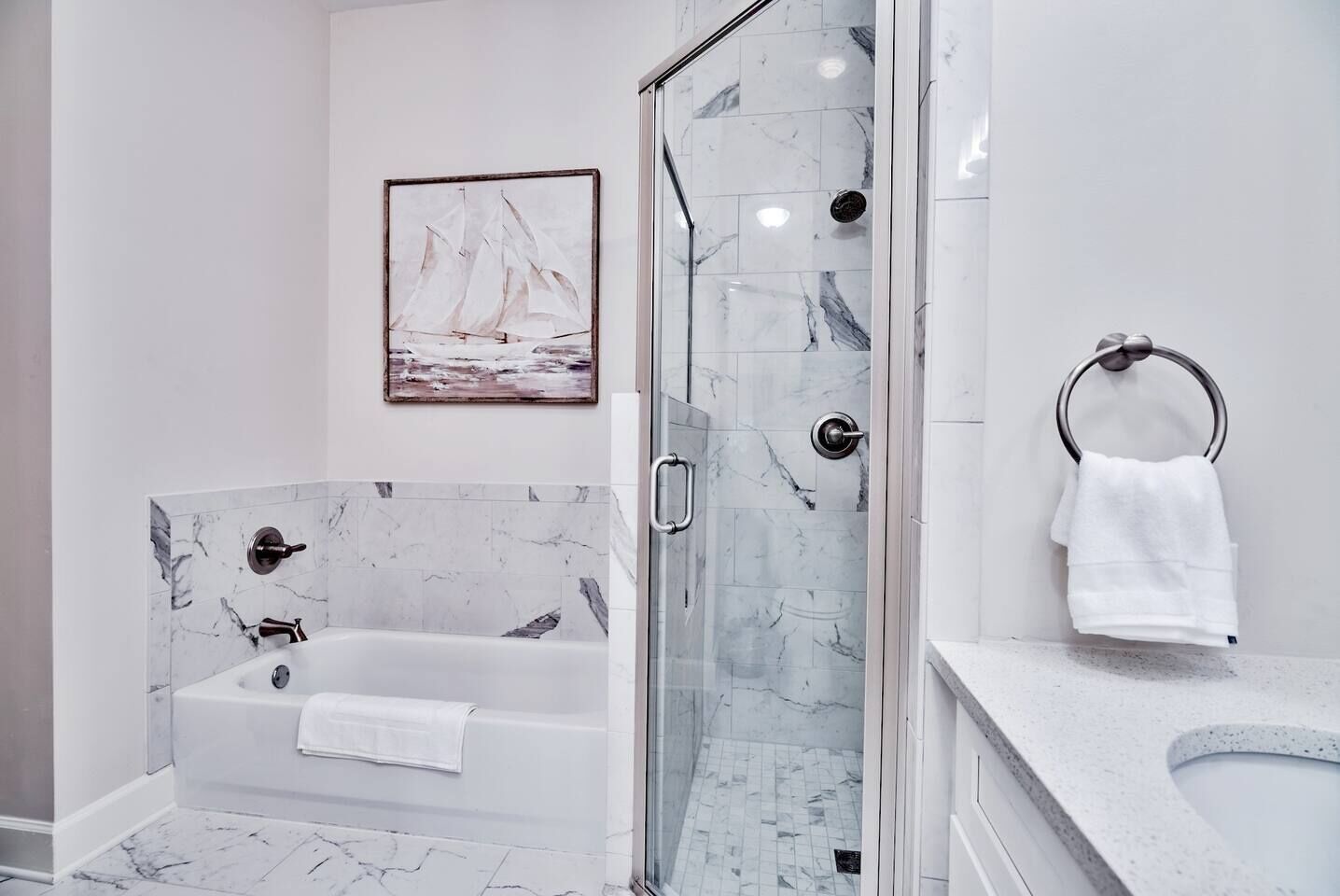 Een moderne badkamer met een douchecabine van glas, een marmeren badkuip en een witte wastafel.