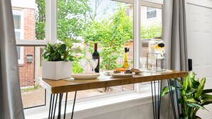 A dining table with plates, glasses, and a bottle, set against a window with a view of a brick building and greenery. - Manoir Highfield (Moncton)