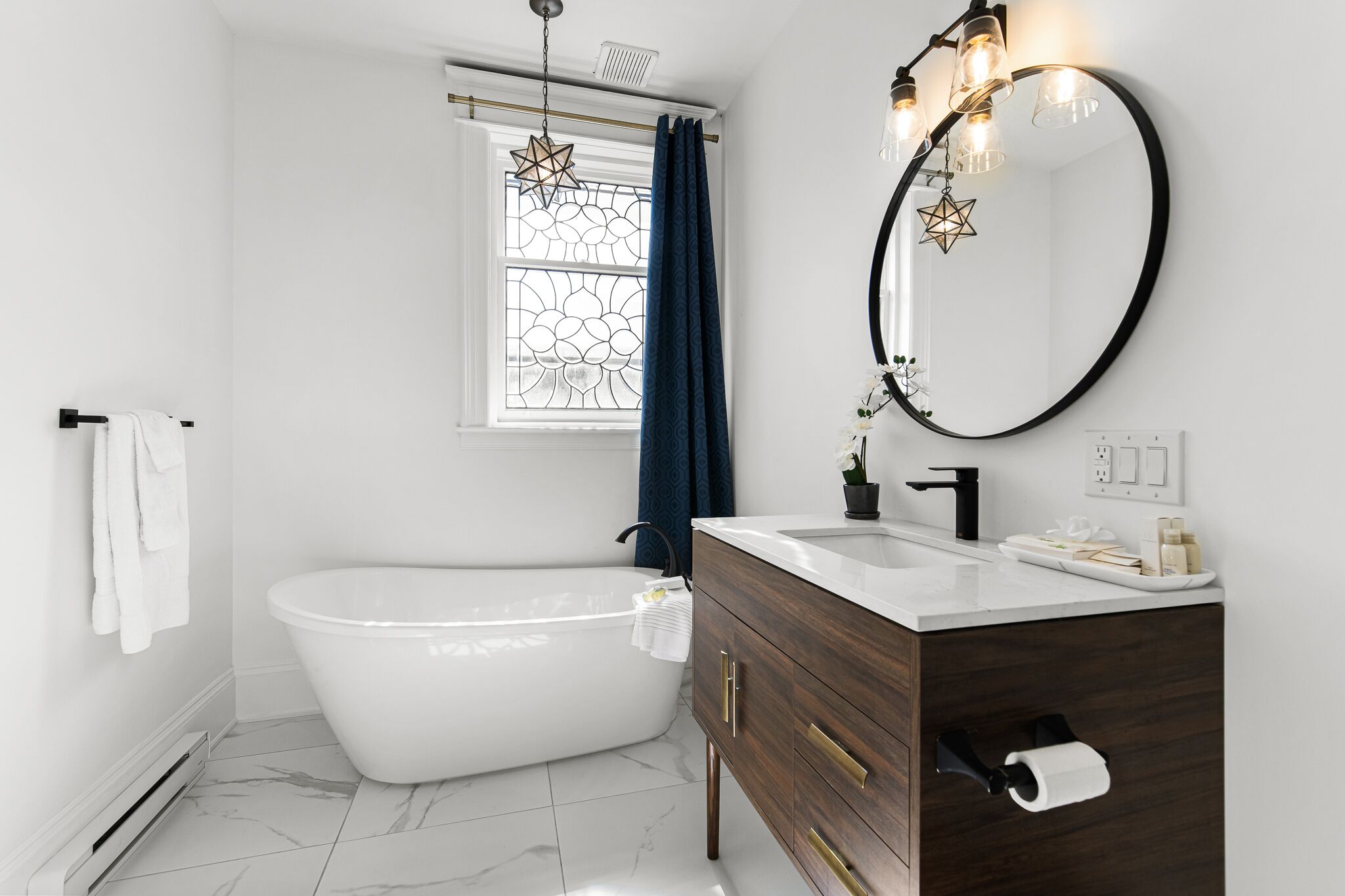 A modern bathroom with a freestanding bathtub, a vanity with a mirror, and a window with decorative glass.