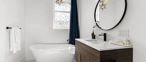 A modern bathroom with a freestanding bathtub, a vanity with a mirror, and a window with decorative glass.