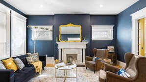 A living room with a fireplace, dark blue walls, and a yellow-framed mirror. - Manoir Highfield (Moncton)