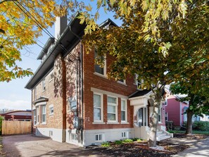 A two-story brick house with a white porch and a garage. - Manoir Highfield (Moncton)