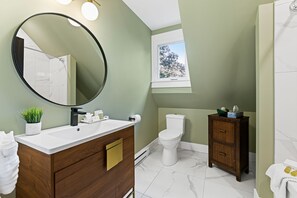 A bathroom with a white sink, a round mirror, a toilet, and a cabinet. - Manoir Highfield (Moncton)