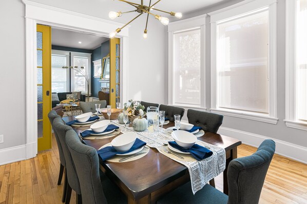 A dining room with a wooden table set for six, surrounded by grey upholstered chairs. - Manoir Highfield (Moncton)