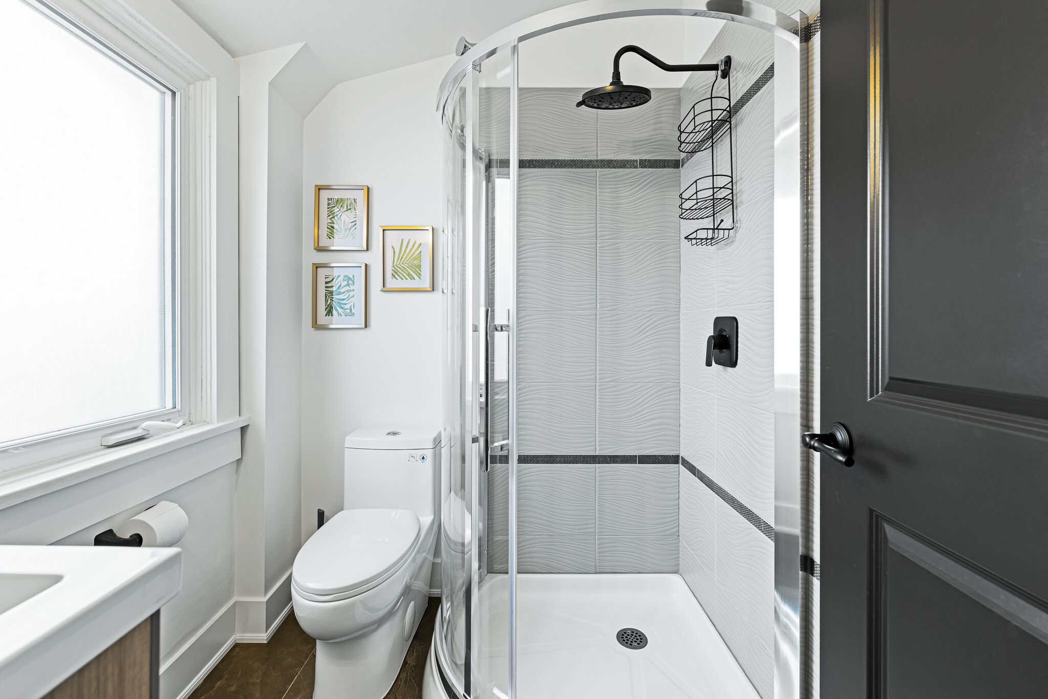 Un baño moderno con inodoro, cabina de ducha y cuadros en la pared.