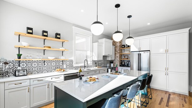 A modern kitchen with white cabinets, a large island, hanging pendant lights, and bar stools. - Manoir Highfield (Moncton)