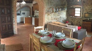A dining area with a table set for four, a kitchen in the background, and a stone wall with a television. - Wonderful private villa with private pool, A/C, WIFI, TV, patio, pets allowed and panoramic view (Monteverdi Marittimo)