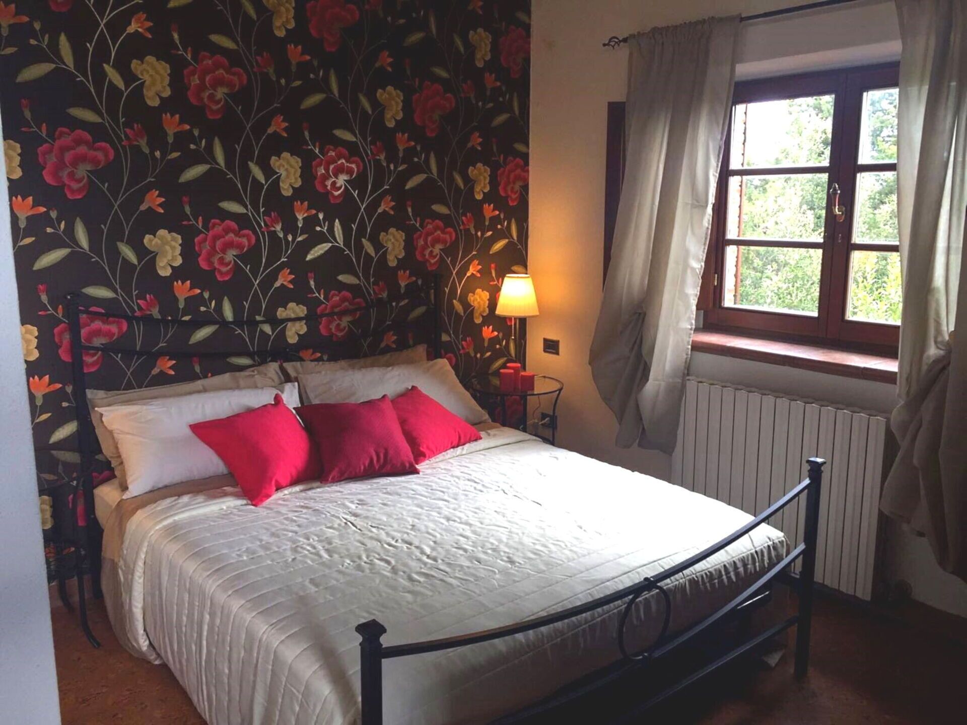 Ein Bett mit floraler Tapete, einer Nachttischlampe und einem Fenster mit Vorhängen.