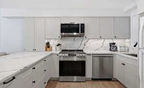 Une cuisine moderne avec des meubles blancs, une cuisinière en acier inoxydable, un four à micro-ondes et une machine à café.