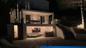 Ein modernes, zweistöckiges Haus mit Swimmingpool, Sitzgelegenheiten im Freien und einer Treppe, die zum oberen Stockwerk führt.