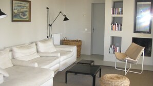 Ein Wohnzimmer mit einem weißen Sofa, einem schwarzen Couchtisch, einem Korbwannenkorb, einem Korbsitzhocker, einer schwarzen Stehlampe und einem Bücherregal mit Büchern.