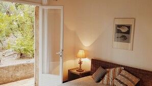 Et soveværelse med seng, et natbord, en lampe, et billede i ramme og en dør, der fører til et udendørs område.