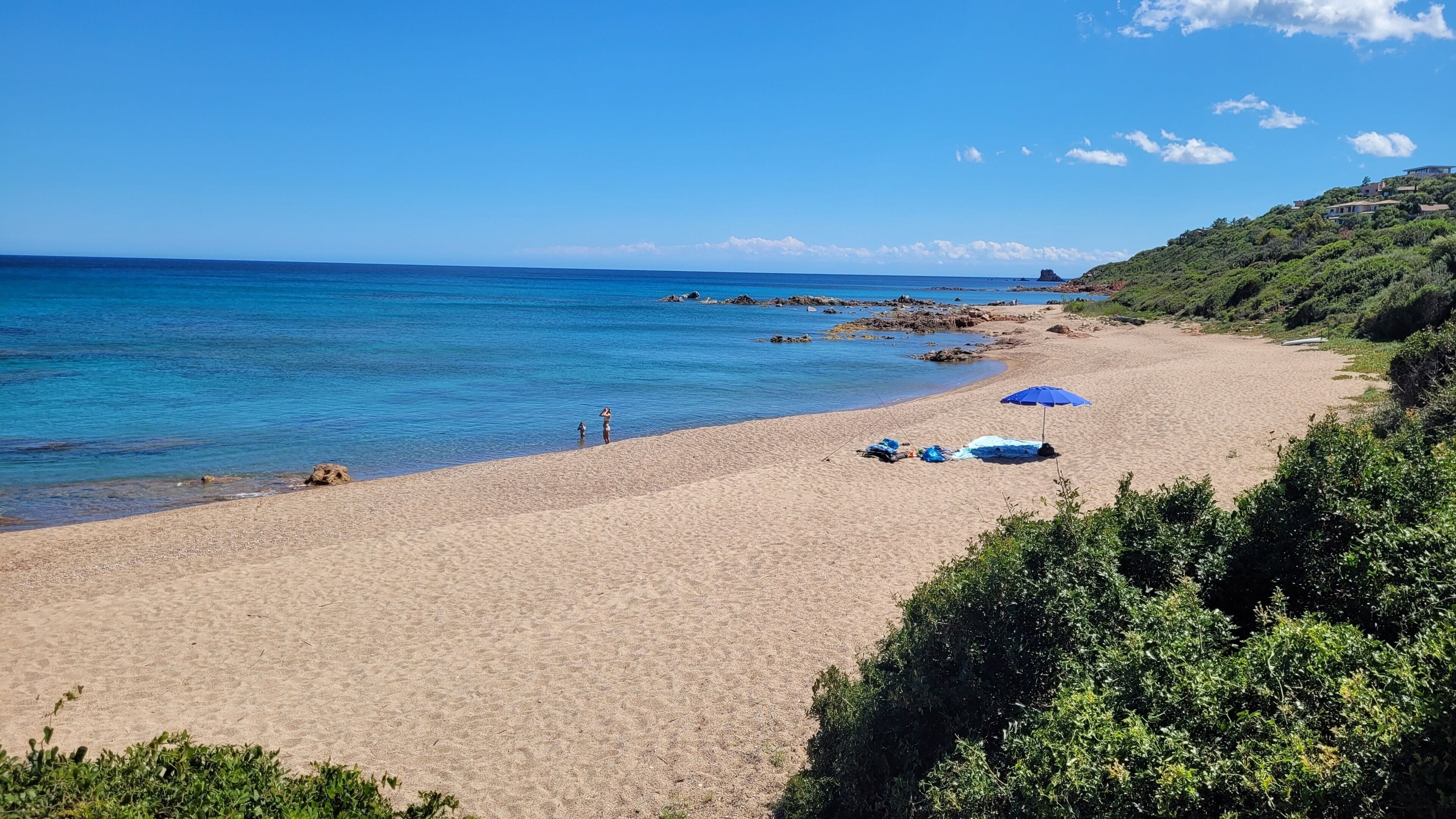 A beach with clear blue water, a sandy shore, and a few umbrellas.