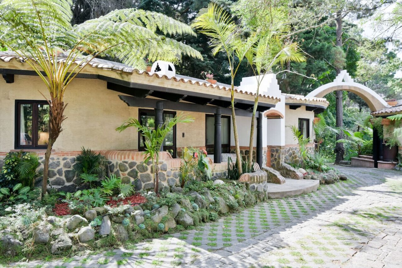A house with a stone facade, a tiled roof, and a garden with various plants and a small waterfall.