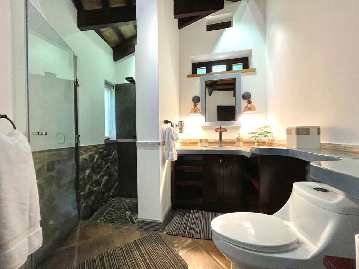 A bathroom with a glass shower enclosure, a toilet, and a sink with a mirror above.