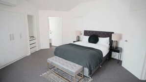 Ein Schlafzimmer mit Bett, Nachttischen, einer Bank, einem Kleiderschrank und einer Tür zu einem anderen Raum.
