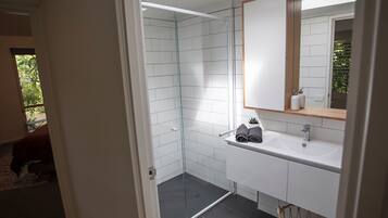 A modern bathroom with white tiles, a glass shower enclosure, a sink with a mirror, and a small potted plant.
