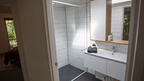A modern bathroom with white tiles, a glass shower enclosure, a sink with a mirror, and a small potted plant.