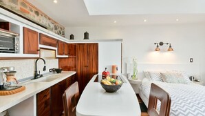 Une cuisine compacte avec des meubles en bois, un plan de travail blanc et un îlot central agrémenté d’un panier de fruits.