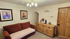 A living room with a brown sofa, a wooden cabinet with decorative items, and two framed pictures on the wall. - Saltburn Holidays Bluebell Cottage (Guisborough)