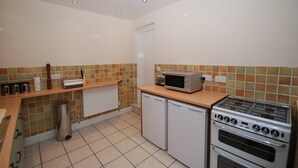 A compact kitchen with a microwave, a small refrigerator, a stove, and a tiled backsplash. - Saltburn Holidays Bluebell Cottage (Guisborough)