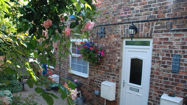 A brick building with a white door, a hanging flower basket, and a small window. - Saltburn Holidays Bluebell Cottage (Guisborough)