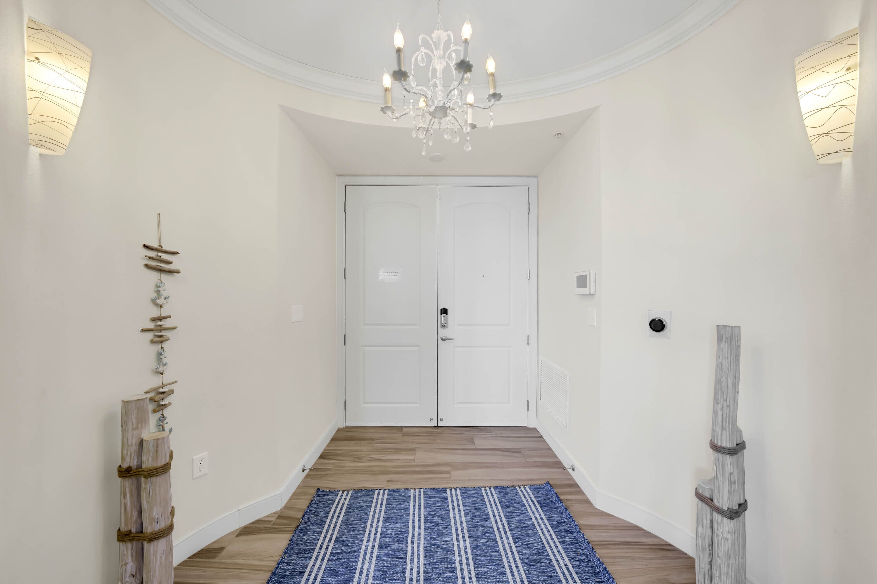 A hallway with a chandelier, white walls, a blue rug, and a wooden sculpture.