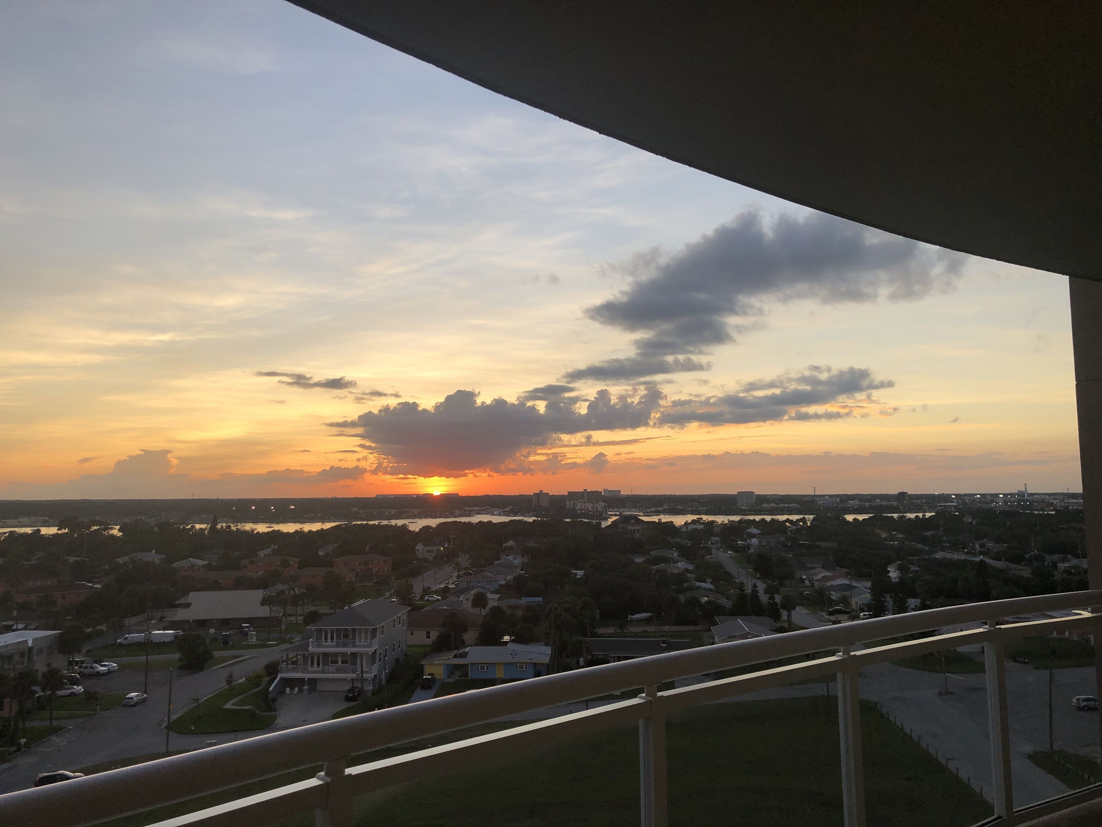 A sunset view from a balcony overlooking a residential area with houses and a body of water.