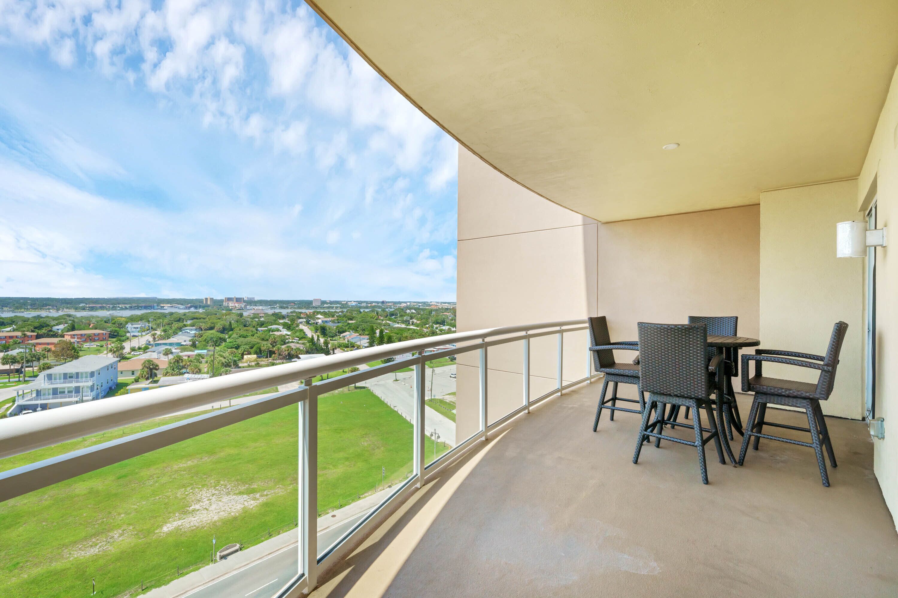 Un balcon donnant sur un paysage urbain, une table avec des chaises et une rambarde.