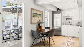 Une cuisine moderne avec des meubles blancs, un réfrigérateur en acier inoxydable et un coin repas comprenant une table et des chaises.