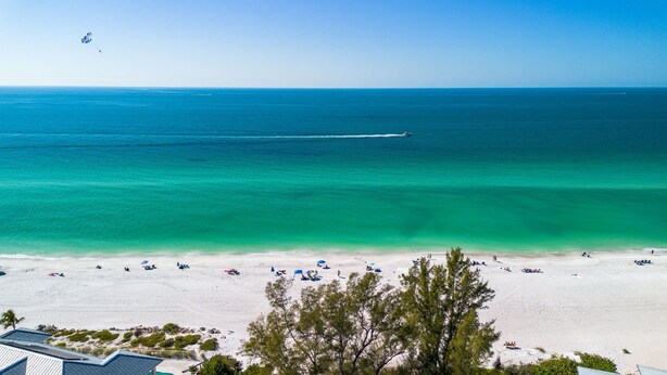Une plage avec une eau turquoise et limpide, du sable blanc et quelques arbres au premier plan.