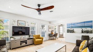 Un salon moderne doté d’un téléviseur à écran plat, d’un ventilateur de plafond, d’un coin repas et d’un tableau représentant une vue sur la plage.