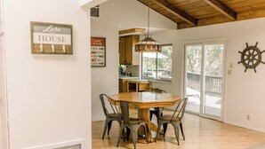 Un comedor con mesa de madera y sillas de metal, una araña y una rueda de barco en la pared.