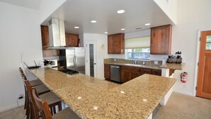 A kitchen with granite countertops, wooden cabinets, stainless steel appliances, and a built-in island with bar seating. - Lake Shore - Lake Front (Bass Lake)